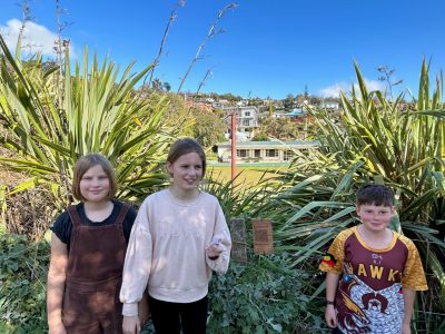 Two girls and a boy standing next to a wooden QR code on a walking track with a school building in the background