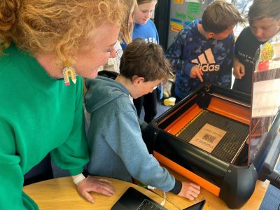 Three boys and a woman looking at a QR code on a 3D printer